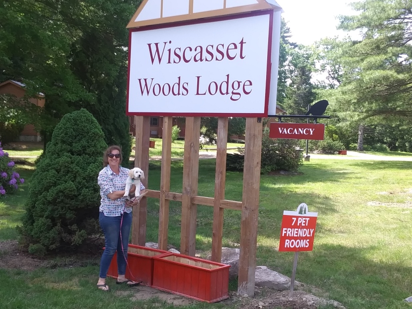 Pet owner with puppy in front of Wiscasset Woods Lodge sign